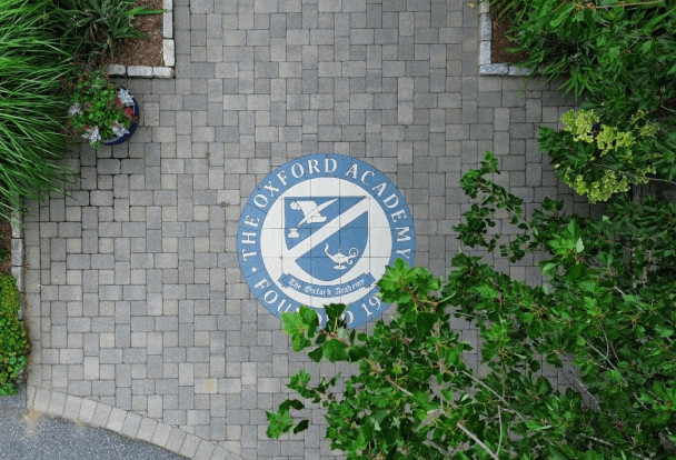 Aerial view of a paved area featuring a circular emblem of the oxford academy, surrounded by green shrubs.