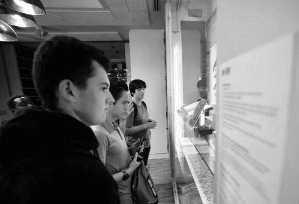 Black and white image of young adults intently reading an exhibit description in a museum.