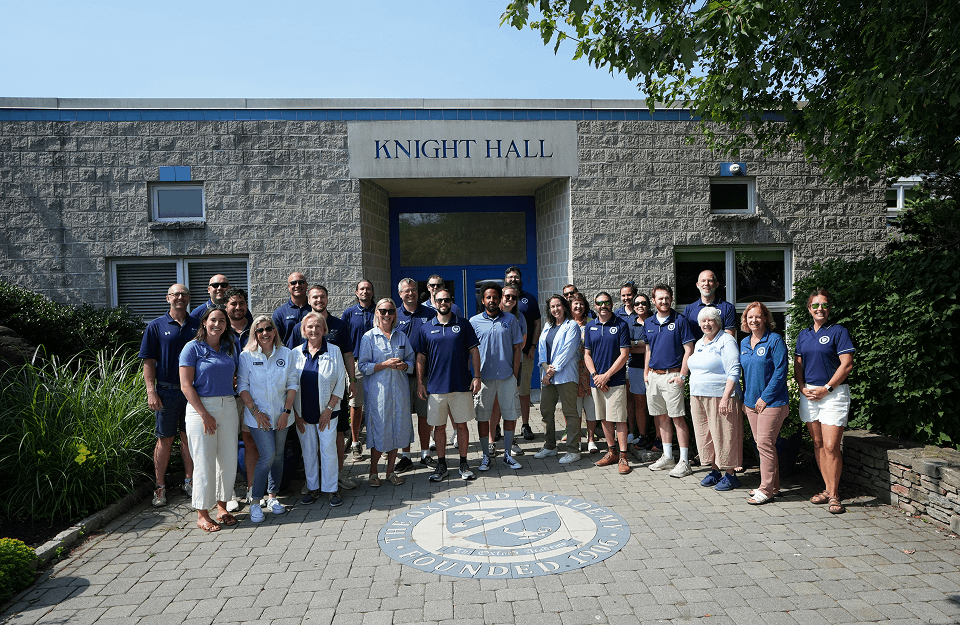 A group of staff and faculty pose for a photo outside a building labeled Knight Hall, standing on a paved area with a crest and surrounded by greenery.